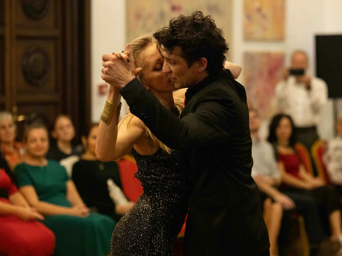 Una pareja de tango baila junto a mesas de cena a la luz de las velas en un entorno teatral (fotografía representativa de una actuación con cena, no de la propia compañía de este espectáculo)