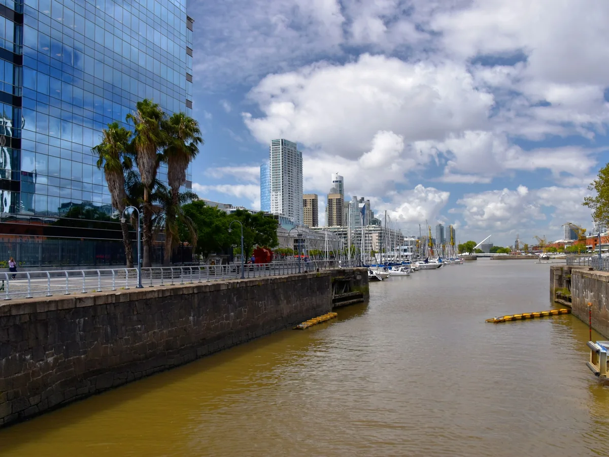 Vel eros amarrados a lo largo de un canal en Puerto Madero, Buenos Aires, con torres de oficinas de cristal tras el muelle
